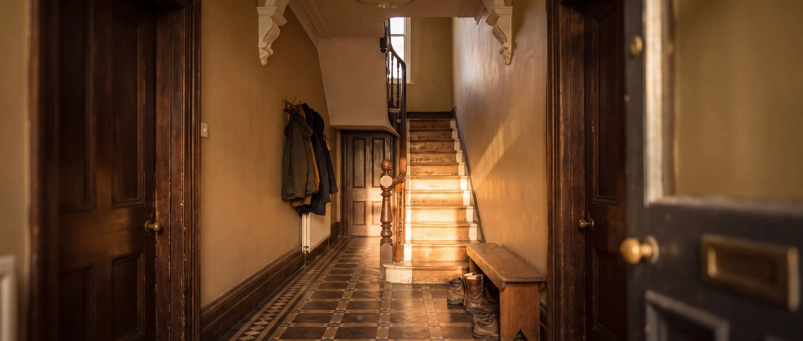 A Victorian hallway with panelled doors, a tiled floor and morning light down the stairs