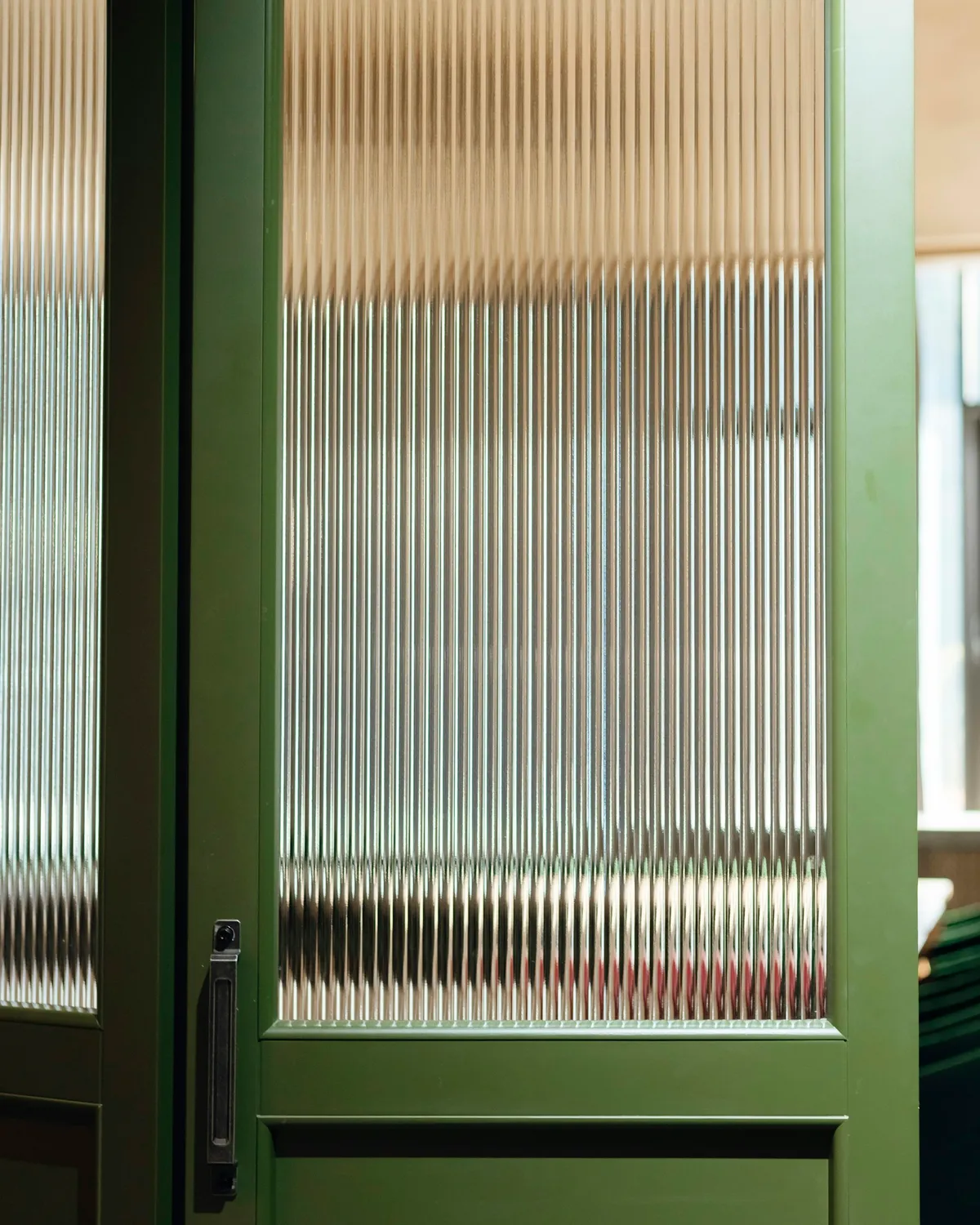 A green-painted door with ribbed glass panels catching the light
